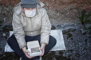 dakloos. een man in gescheurde kleren en een medisch masker bedelt. covid19. foto