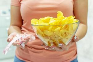 een bord chips en een centimeter tape in de handen van het meisje. junk food. het concept van de strijd tegen overgewicht. selectieve aandacht, filmkorrel. foto