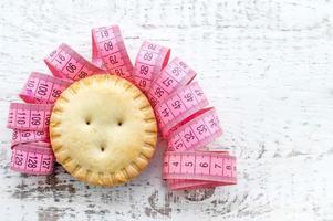 cupcake met een roze centimeterlint in de vorm van haar op een witte houten achtergrond. het concept van de strijd tegen overgewicht foto