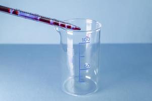 medisch laboratorium. bloed uit een pipet wordt in een lege reageerbuis op een blauwe achtergrond gegoten. laboratorium testen. foto