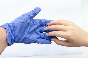 de hand van een man in blauwe steriele handschoenen begroet de hand van een man zonder handschoenen op een witte achtergrond. het concept van bescherming tegen virussen. selectieve aandacht. foto