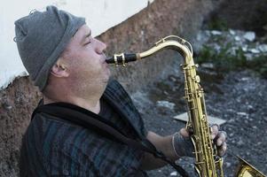 een dakloze straatmuzikant zit op straat met een saxofoon om eten te verdienen. foto