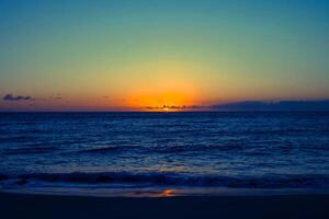 zonsondergang oranje in zee en hemelsblauw prachtige zee en zonsondergang met grote gele zon onder de heuvels van het zeeoppervlak op de achtergrond. foto