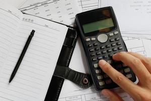 besparingen, financiën, economie en kantoorconcept - close-up van de mens met rekenmachine die aantekeningen maakt, pen op het notitieboek en rekening op het bureau, gegevensanalyse, zachte focus. foto