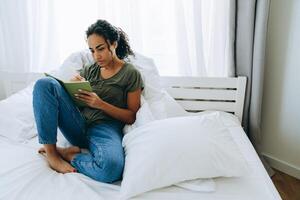 peinzende afrikaanse vrouw die iets in kladblok op het bed schrijft foto