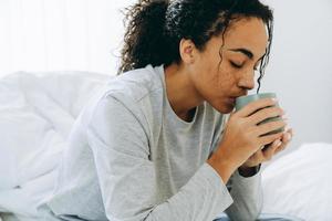 Afrikaanse vrouw die koffie drinkt op het bed