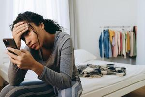 jonge zwarte vrouw die mobiele telefoon gebruikt terwijl ze op bed zit foto