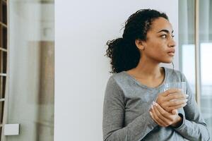 jonge zwarte vrouw die water drinkt tijdens tijd thuis doorbrengen? foto
