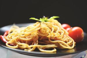 spaghetti pasta en tomaat chili en basilicum laat traditioneel heerlijk Italiaans eten spaghetti bolognese op bord op de eettafel met zwart foto