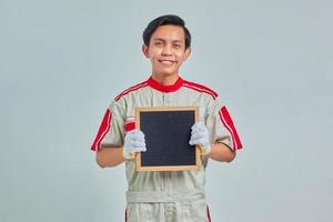 portret van een vrolijke jonge monteur die uniform draagt met een leeg bord op een grijze achtergrond foto