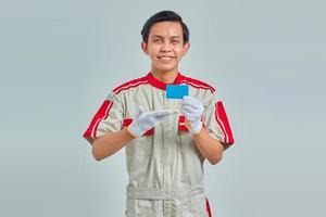 portret van knappe jonge monteur die creditcard met palm toont met lachende uitdrukking op grijze achtergrond foto