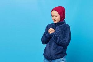 aantrekkelijke jonge aziatische vrouw bidt en sluit haar ogen op blauwe achtergrond