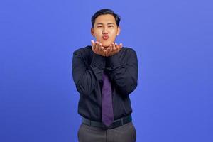portret van een charmante jonge aziatische man die handpalmen vasthoudt en luchtkus stuurt op een paarse achtergrond foto