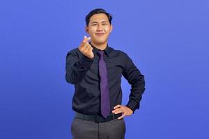 glimlachende jonge aziatische man die een teken van een liefdesgebaar op een paarse achtergrond toont foto