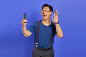 portret van een gelukkige jonge aziatische man die een mobiele telefoon gebruikt met de hand zwaaiend naar de smartphone foto