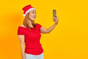 vrolijke jonge aziatische vrouw met een kerstmuts die videogesprek voert op gele achtergrond foto