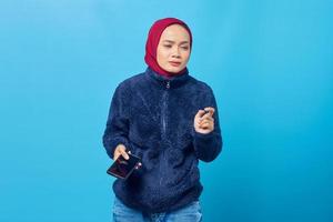 verwarde jonge aziatische vrouw die smartphone op blauwe achtergrond gebruikt foto