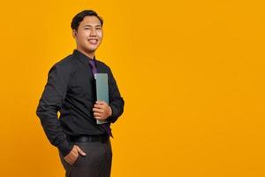 Glimlachende knappe jonge zakenman die laptop knuffelt en naar de camera kijkt op gele achtergrond foto