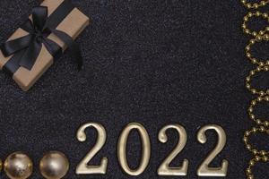 nieuwjaar 2022. bovenaanzicht nieuwjaarsmodel op zwart glanzend rood lint als achtergrond, geschenkdoos, gouden cijfers en veelkleurige glitters. lay-out van ansichtkaarten foto