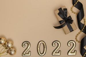 nieuwjaar 2022. bovenaanzicht nieuwjaarsmodel op beige achtergrond zwart lint, geschenkdoos, gouden cijfers en veelkleurige sparkles. lay-out van ansichtkaarten, uitnodigingen. foto