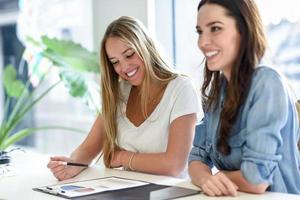 twee jonge vrouwen die afbeeldingen op een wit bureau bestuderen foto