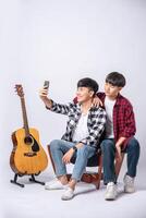 twee liefdevolle jonge mannen zitten op een stoel en nemen een selfie vanaf een smartphone. foto