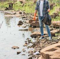 een man met oranje handschoenen die afval verzamelt in een zwarte zak. foto