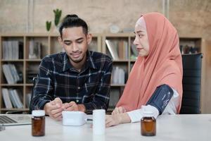 mensen medische kliniek verzekering levensstijl. een minnaar van een jong moslimpaar doet thuis zijn gezondheidscontroles. de man geeft om de gezondheid van zijn vrouw, die een mooie vrouw is die een hijab draagt. foto