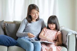 gelukkige Aziatische moeder die haar schattige dochter leert om thuis in de woonkamer te studeren