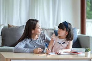 Aziatische moeder leert haar schattige dochtertje om thuis in de woonkamer te studeren foto