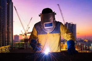 industriële werknemer lassen staalconstructie voor infrastructuur bouwproject met bouwplaats op de achtergrond. foto