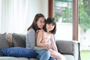 Aziatische moeder voelt geluk tijdens het knuffelen van haar schattige dochter met liefde en zorg thuis foto