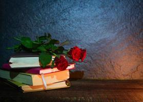 rode roos en boek liefdesonderwijs en liefde op school concept - stilleven bloemen op een oud boek in de donkere achtergrond foto