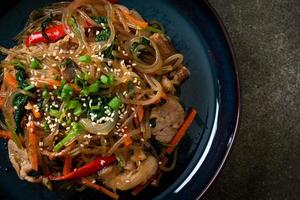 japchae of geroerbakte Koreaanse vermicelli noedels met groenten en varkensvlees gegarneerd met witte sesam foto