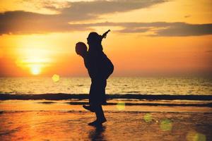 Aziatische geliefden blij op het strand met een prachtige zonsondergang op de achtergrond man die de vrouw optilt. foto