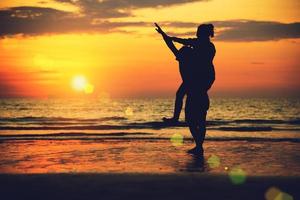 Aziatische geliefden blij op het strand met een prachtige zonsondergang op de achtergrond man die de vrouw optilt. foto