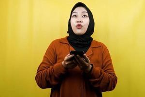mooie jonge Aziatische moslimvrouw geschokt, verrast, wow-uitdrukking, smartphone in de hand, omhoog kijkend, geïsoleerd foto