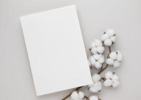 wit uitnodigingskaartmodel met een katoenen bloem op beige achtergrond, minimale beige werkpleksamenstelling, plat gelegd, mockup