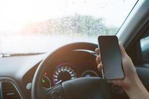 hand van vrouw op stuur een auto besturen tijdens het gebruik van smartphone. foto