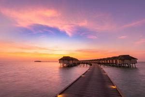 geweldig zonsondergangpanorama op de Malediven. luxe resort villa's zeegezicht met zachte led-verlichting onder kleurrijke lucht. mooie schemerhemel en kleurrijke wolken. mooie strandachtergrond voor vakantievakantie