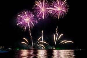 geweldig mooi kleurrijk vuurwerk op de feestavond, te zien op het zeestrand met veelkleurige reflectie op water foto