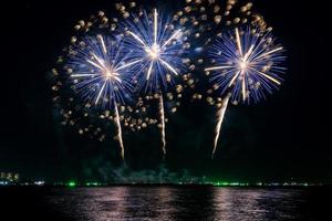 geweldig mooi kleurrijk vuurwerk op de feestavond, te zien op het zeestrand met veelkleurige reflectie op water foto