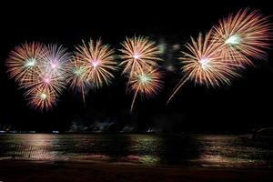 geweldig mooi kleurrijk vuurwerk op de feestavond, te zien op het zeestrand met veelkleurige reflectie op water foto