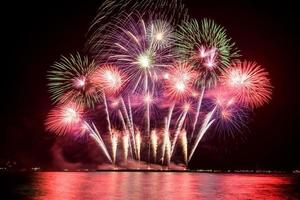 geweldig mooi kleurrijk vuurwerk op de feestavond, te zien op het zeestrand met veelkleurige reflectie op water foto