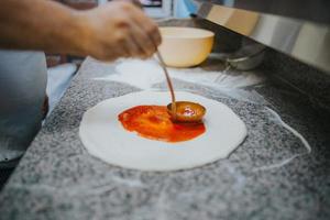 man zet tomatensaus op pizzadeeg foto