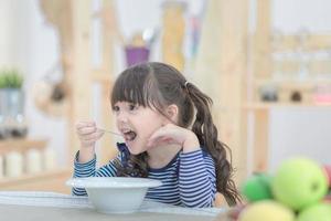 schattig klein meisje dat 's ochtends ontbijt met cornflakes en melk eet. fotoserie van familie, kinderen en gelukkige mensen concept. foto