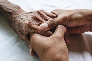 handen van de oude man en een mannenhand op het witte bed foto