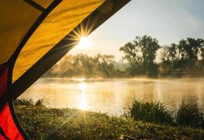 zonsopgang sunflare een piek door de opening van de tent in een landschap van oekraïne en de rivier met mist in de buurt. foto