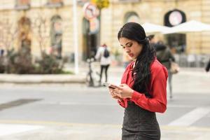 Spaanse stewardess op stedelijke achtergrond die naar haar mobiele telefoon kijkt foto