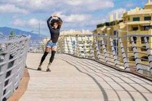 Afro kapsel vrouw op rolschaatsen buiten rijden op stedelijke brug foto